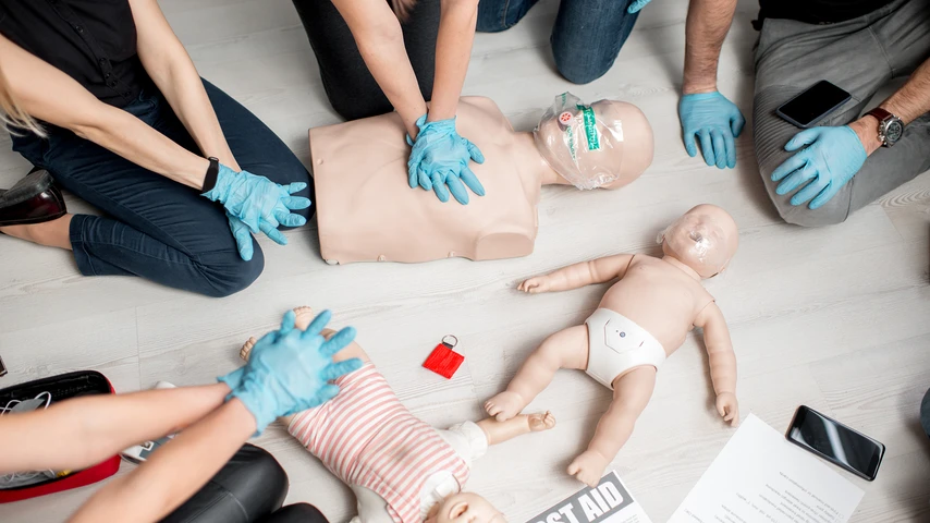 Group of people learning how to make first aid heart compressions with dummies during the training indoors